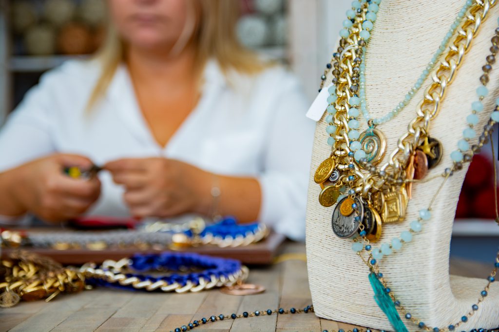 Stand with handmade necklaces and craftswoman working and making handmade jewelry in small business workshop