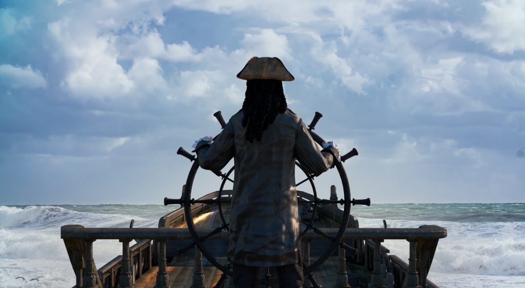 the pirate captain holds the ship's steering wheel and sails across the sea on a sailing pirate ship render