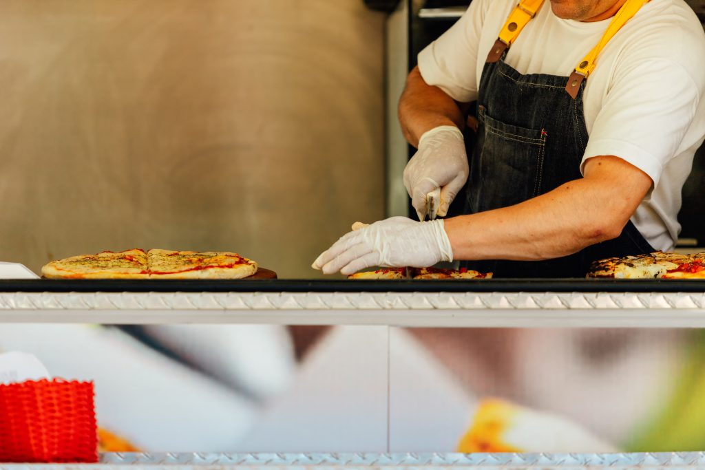 Pizzaman cuts slices of pizza on the counter of a food truck